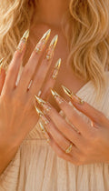 May include: Gold-colored nail covers with a pointed design. The nail covers have a decorative filigree design with small, clear stones. The nails are long and elegant, and the overall look is glamorous and stylish.
