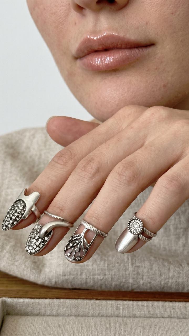 May include: Silver nail rings in various designs. One ring features a pointed shape with embedded crystals, another has a curved design with crystals, and a third has a floral design. A fourth ring has a round crystal.