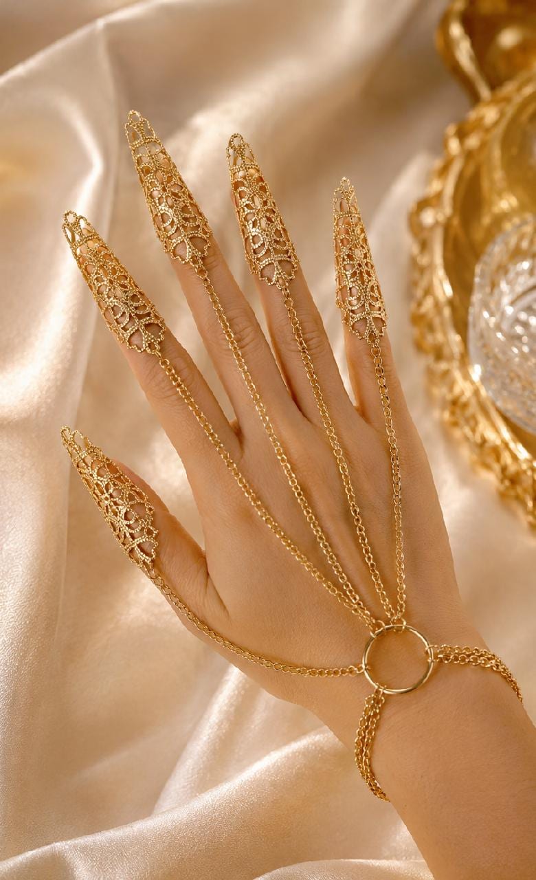 May include: Gold-colored finger rings connected by delicate chains to a bracelet. The rings feature an intricate, openwork design. The jewelry is displayed on a cream-colored satin surface, creating an elegant aesthetic.